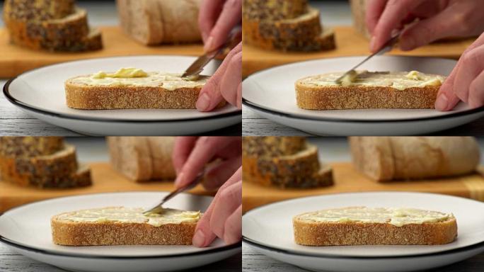 女性用刀将黄油涂在一片面包上。背景中模糊的两种面包。滑块镜头，4K