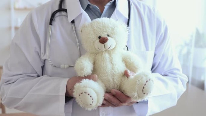 高级男性普通儿科医生手里拿着泰迪熊，特写