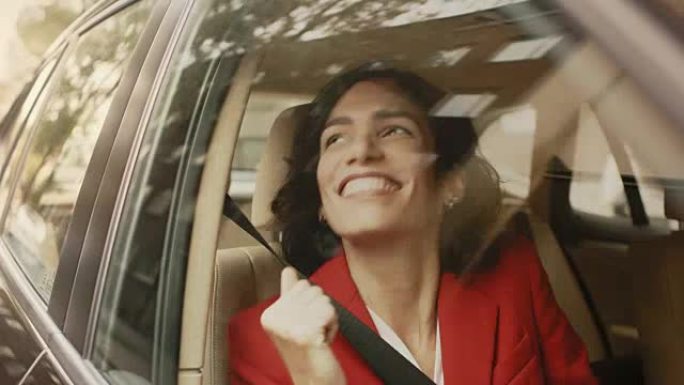 美丽的幸福女人坐在汽车的乘客座位上，她很开心，跳舞。大城市的景色反映在窗口中。摄像机安装在移动汽车外