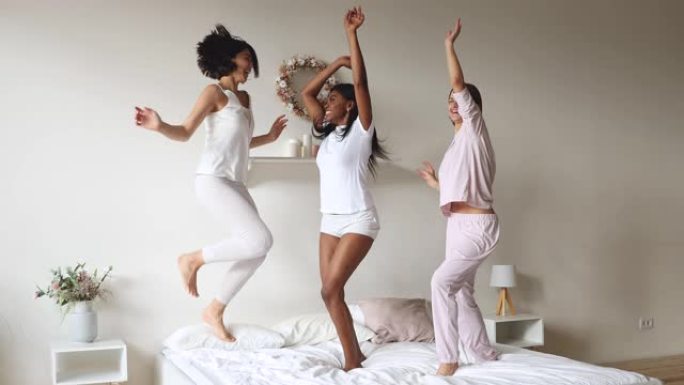 三个无忧无虑的多样化女士穿着睡衣在床上跳跳舞
