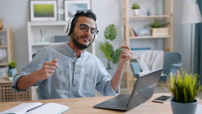英俊的年轻阿拉伯人喜欢在家里用笔记本电脑工作的耳机里听音乐