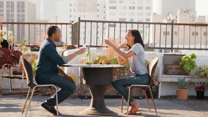 夫妇在屋顶露台上喝酒和吐司，背景是城市天际线