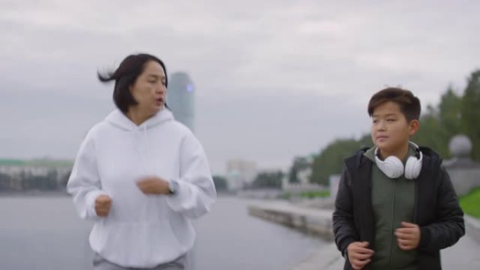 亚洲母亲和儿子在城市的河边奔跑