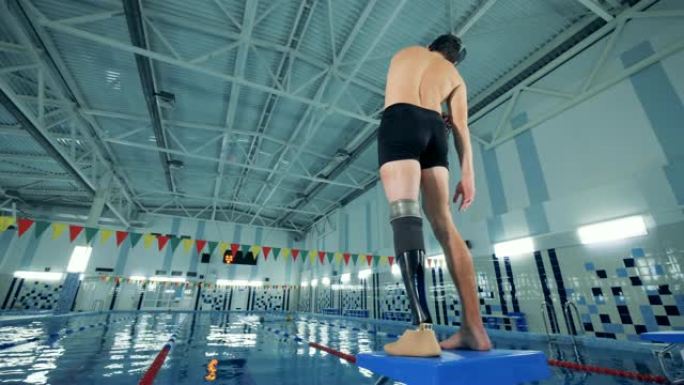 一名残疾游泳者在游泳池附近热身，后视图。