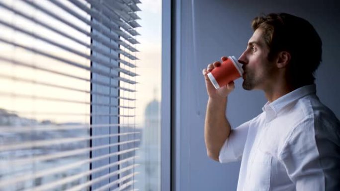 现代办公室4k窗口附近年轻白人男性高管喝咖啡的侧视图