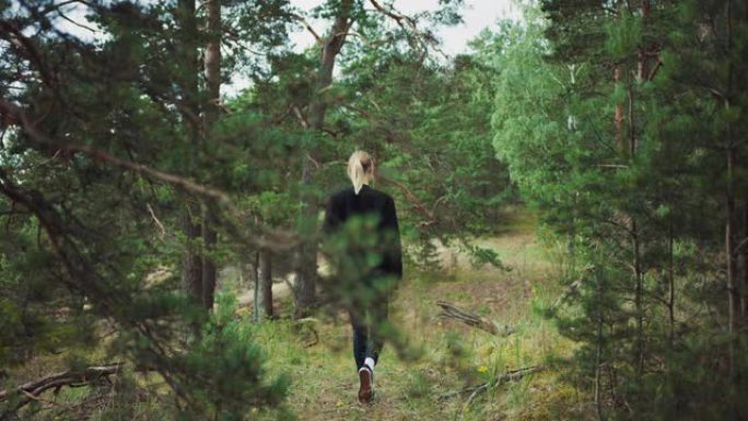一个年轻美丽的金发女人在浪漫的自然氛围中的肖像。女孩穿着黑色衣服，正在森林里散步。她自信满满，独自走