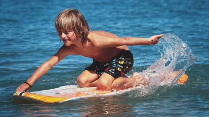 男孩跪在冲浪板上，在海里划水