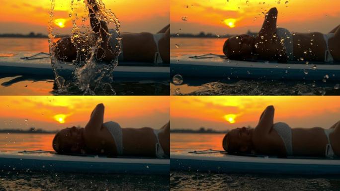 超级SLO MO快乐的女人在日落时在冲浪板上放松时泼水