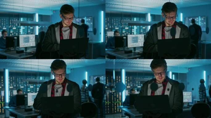 一个戴着眼镜的聪明专注的年轻人拿着笔记本电脑的肖像。在后台技术部办公室，有专家工作和功能数据服务器机