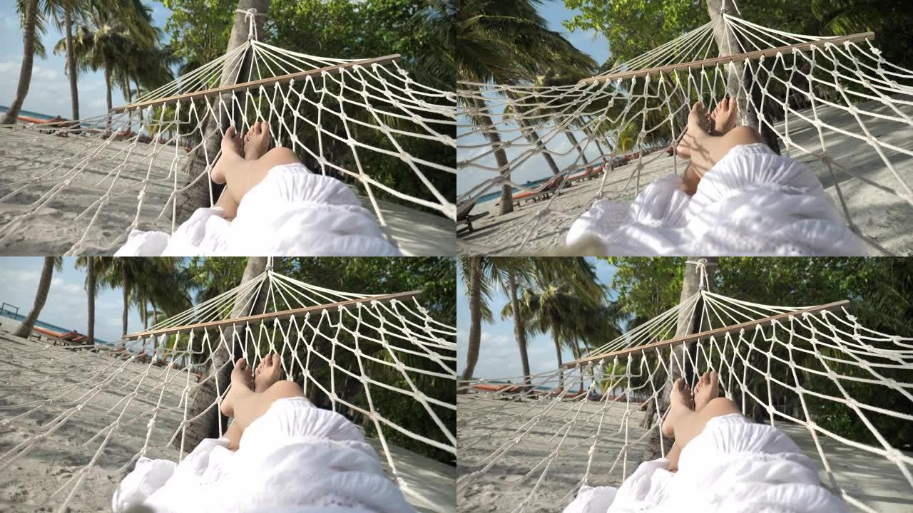 暑假在海滩的吊床上放松的女人的观点腿