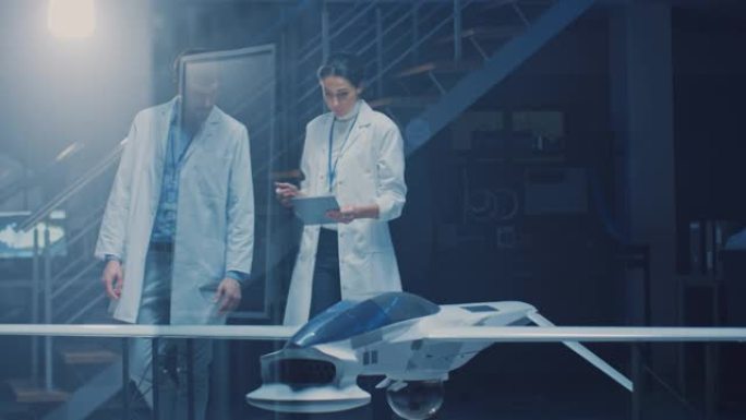 两名航空航天工程师在无人飞行器/无人机原型上工作。穿着白大褂说话的航空科学家，使用平板电脑。带有商用