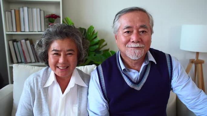 快乐的亚洲老年夫妇享受生活。浪漫的高级夫妇坐在家里的沙发上笑。