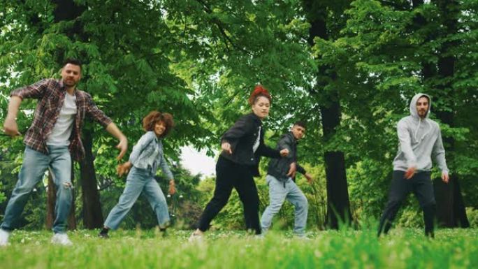一群不同种族的年轻城市舞者的慢动作在阳光明媚的日子里在绿色的城市公园里训练