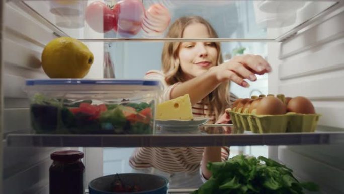 美丽的年轻女子打开装满有机食品的冰箱，在一个纸板可回收的盒子里抓一盒鸡蛋。饮食和健康的生活观念。冰箱