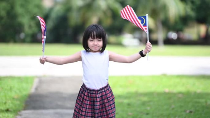 一位亚洲华裔女孩在公园里挥舞着马来西亚国旗，看着镜头