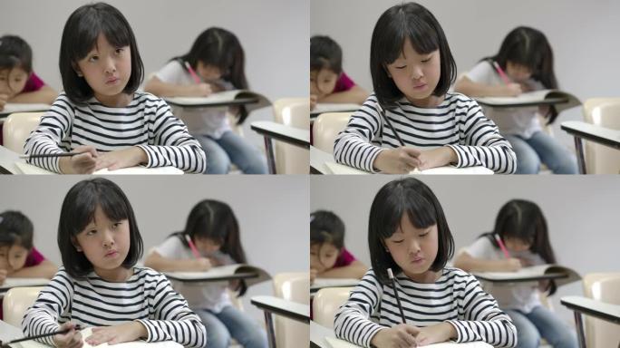 亚洲小女孩在笔记本上写字，在教室里考试。