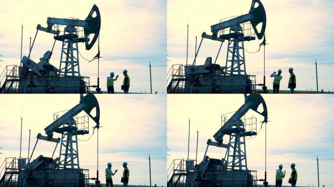 石油井架，石油钻机，油泵附近的两名男性工人的讨论过程。工作油泵，背景上的石油钻机。