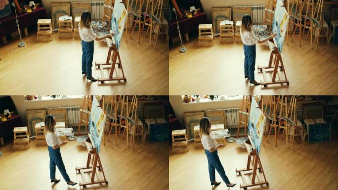 专业画家在工作室绘画中独自在室内工作的高角度视图，然后退后一步评估她的作品。人员和工作空间概念。