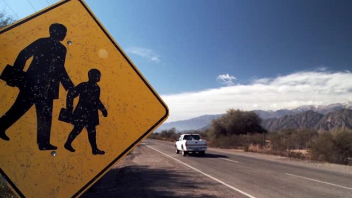 学校区域标志。在阿根廷安第斯山脉附近的一条乡村道路上，一个黄色的警告学校的儿童过马路标志。