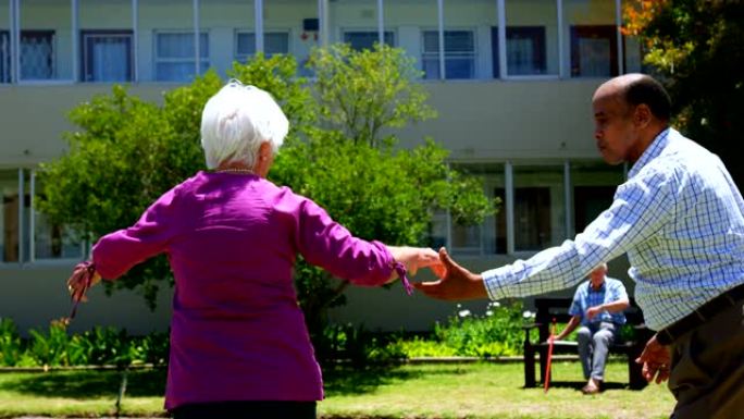 活跃的混血高级夫妇在养老院4k花园中跳舞的侧视图