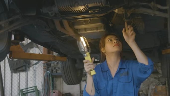 女汽车修理工在车库检查汽车底盘路，汽车服务理念。