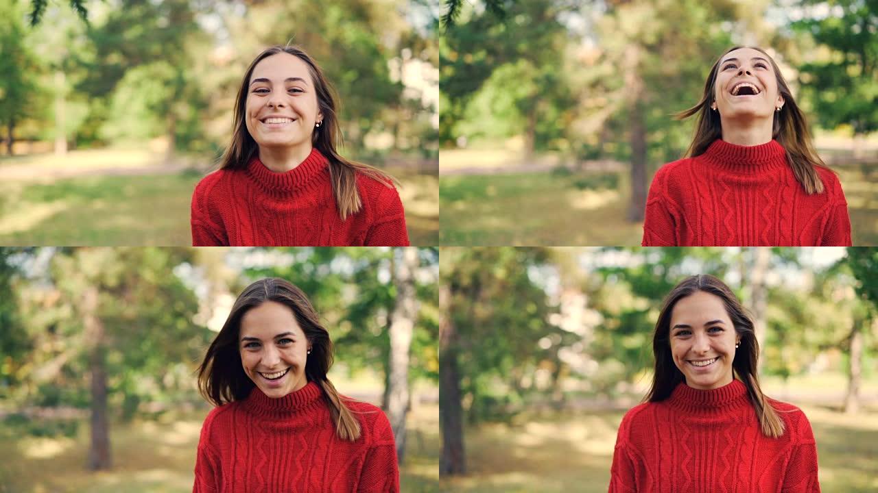 穿着温暖毛衣的开朗女孩的慢动作肖像站在公园里，笑容灿烂，笑着看着相机。自然和千禧一代的概念。