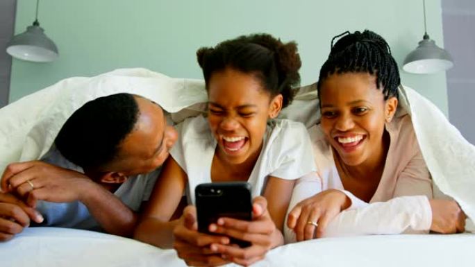 快乐黑人家庭在舒适的家庭4k床上使用手机的前视图