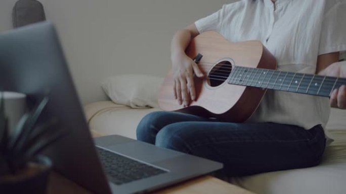 微笑的年轻女子坐在床上，吉他看着笔记本电脑