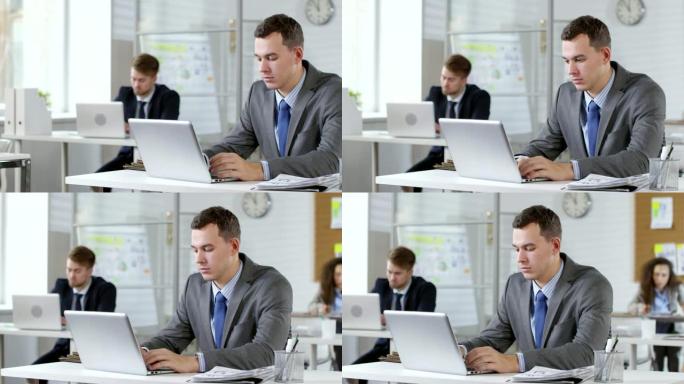 年轻的男性上班族在桌子上的笔记本电脑上打字