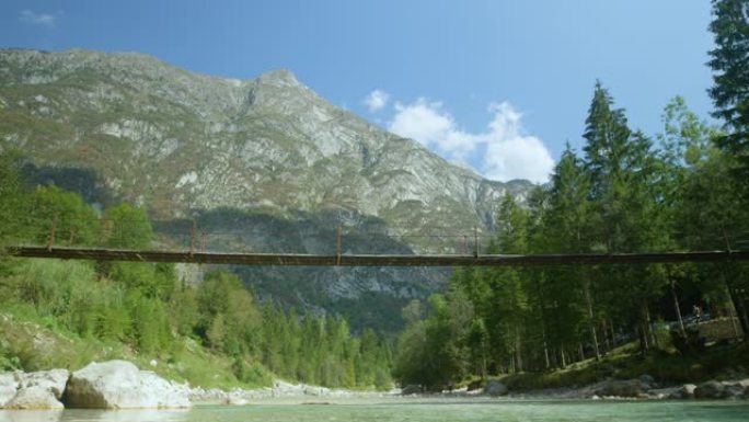 低角度: 悬索桥穿过绿色山谷中宁静的玻璃状小溪。
