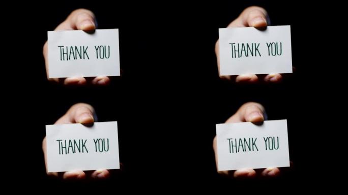 一只手显示一张卡片，上面写着: “谢谢”，孤立在黑色背景上。