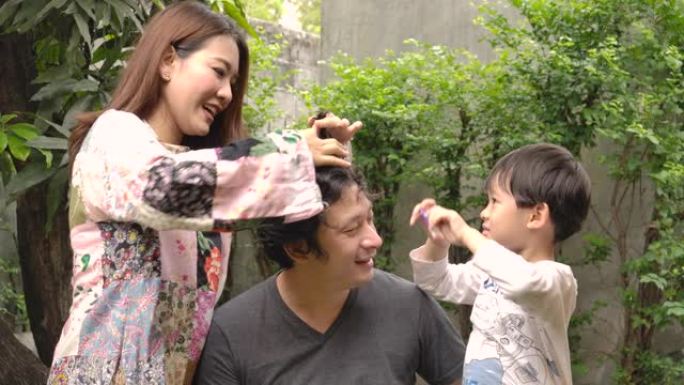 幸福的家庭年轻的亚洲妇女和她的儿子试图在家里用剪刀为她的丈夫理发，因为封锁。居家隔离冠状病毒大流行预