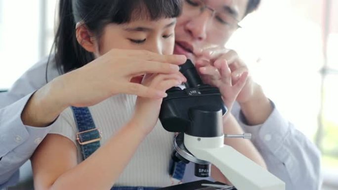 亚洲小孩，老师在学校实验室里用显微镜看。小女孩用显微镜学习科学课。教育主题