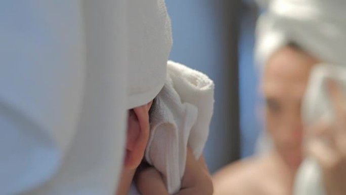 快乐的年轻女子，皮肤干净，头上用白毛巾洗脸。年轻女子在浴室用毛巾擦脸。痤疮