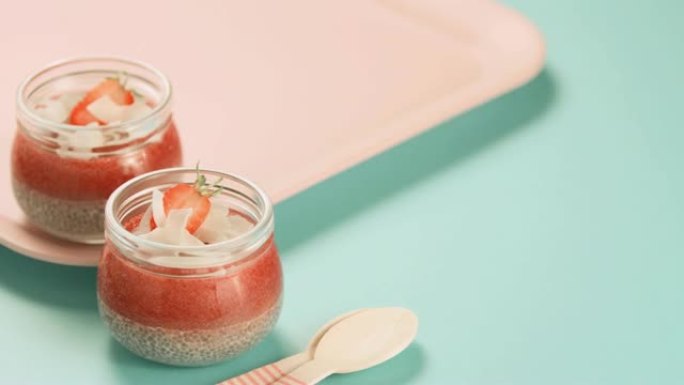 Chia布丁，罐子里有新鲜草莓。薄荷色背景上有浆果的木勺。健康饮食的概念。简单的早餐