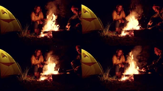 炉火边的年轻夫妇。背景中的帐篷。山地景观