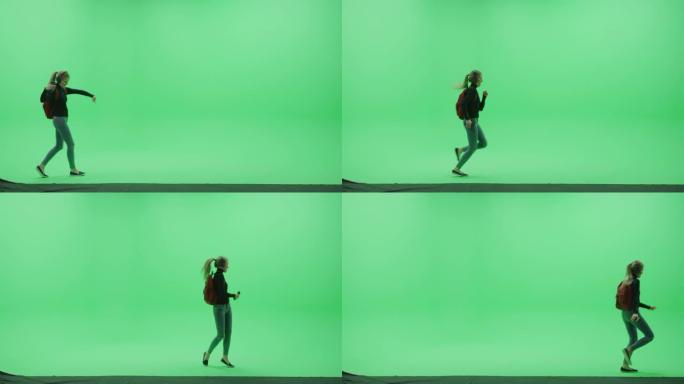绿屏工作室: 美丽的年轻女子戴着背包和耳机，使用智能手机听音乐或播客在色度钥匙室快乐地跳舞