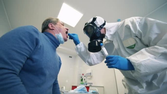 一名男性患者的口腔拭子正在由一名护理人员服用。医生在附近保护冠状病毒病人。