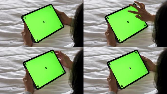 年轻女子躺在床上看着绿色屏幕的数字平板电脑