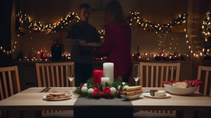 一对年轻夫妇在厨房里摆了一张圣诞餐桌。他们通过智能手机向朋友发送消息。