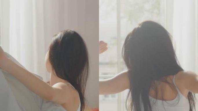 美丽的黑发女人在早上慢慢醒来，伸展身体，从床上站起来，阳光从大窗户照在她身上。垂直屏幕方向9:16的