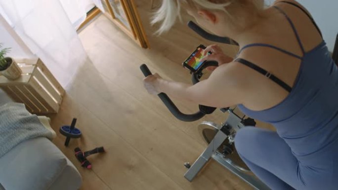 SLO MO女人使用移动应用程序在家中进行健身车训练