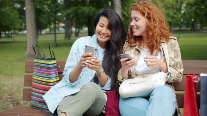 快乐的女孩一起在公园的长凳上使用智能手机聊天放松
