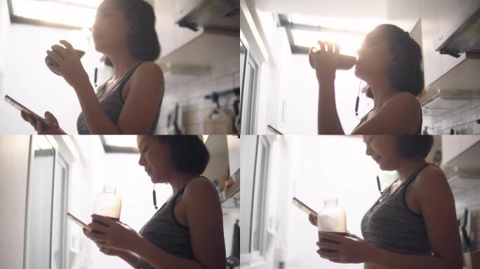 年轻的亚洲妇女在家锻炼后喝蛋白质奶昔。