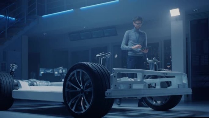 汽车工程师在电动汽车平台底盘原型上工作，使用平板电脑和3D cad软件建模。创新设施: 带车轮、发动