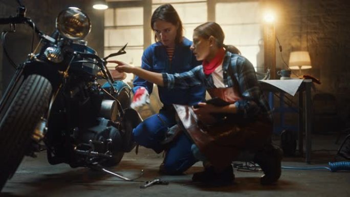 两个年轻漂亮的女性正在讨论定制的Bobber摩托车上所做的工作。才华横溢的女孩使用平板电脑。他们精神