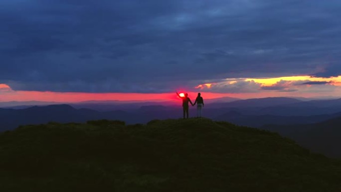 这对夫妇带着烟花棒站在日出背景的山上