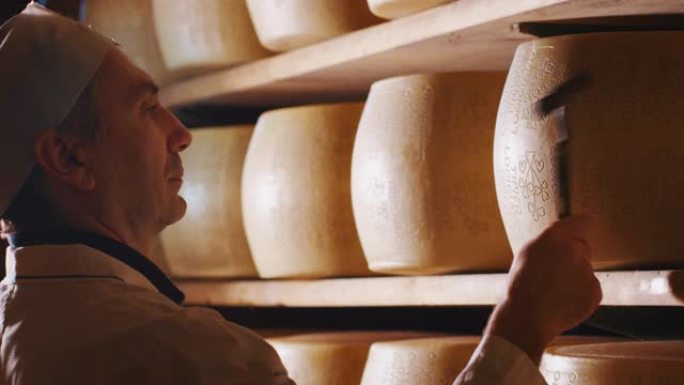 奶酪制造商的慢动作关闭正在控制帕尔马干酪的调味料，该干酪因意大利古老传统而成熟了许多个月