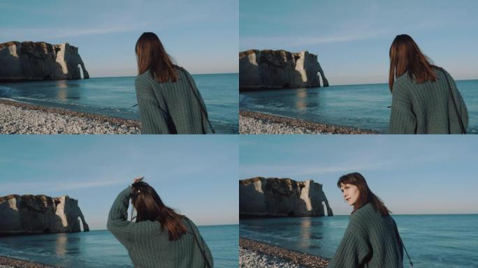 快乐美丽的黑发旅游女人，带着相机探索诺曼底阳光明媚的卵石海滩慢动作。