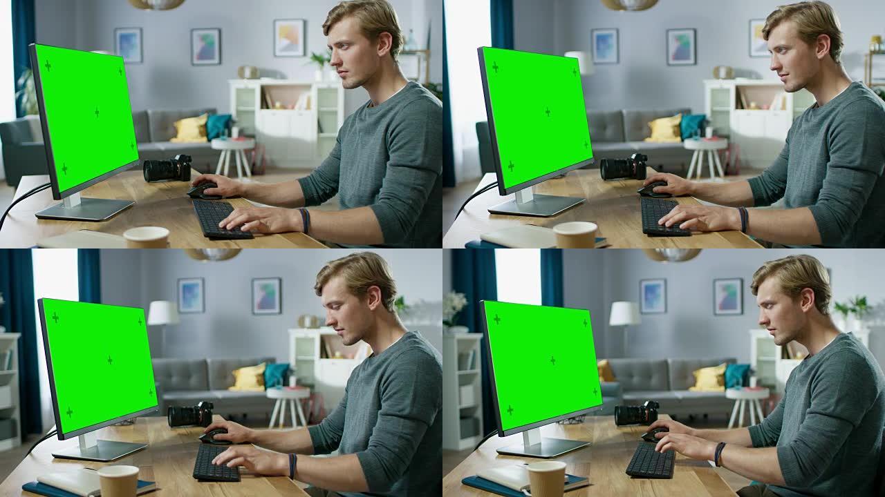 英俊的年轻摄影师坐在舒适公寓的办公桌前，在绿色模拟屏幕个人电脑上工作。